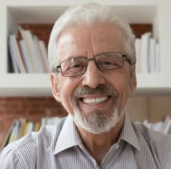 Smiling senior man with glasses in a home library setting.