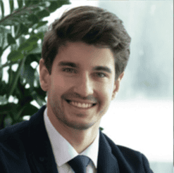 Smiling man in business attire with a plant background.
