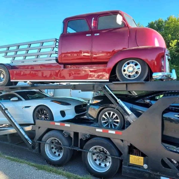 Vintage red truck being transported on a car carrier trailer.