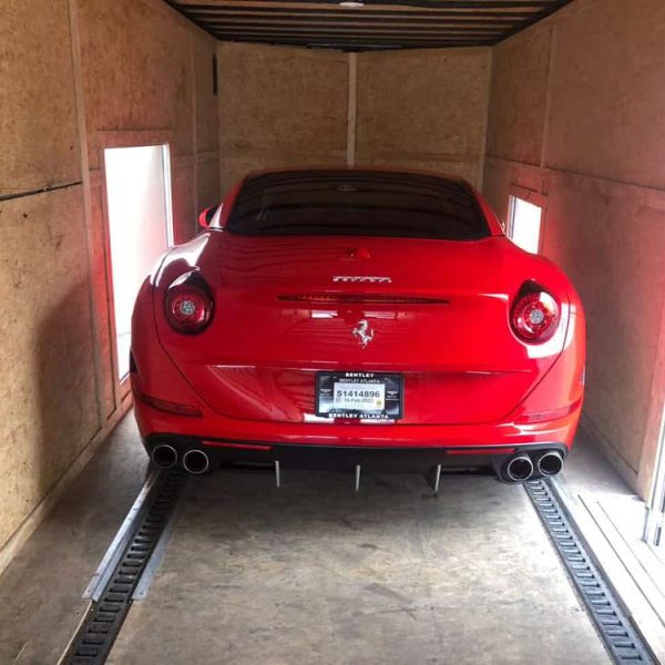 Red Ferrari inside a shipping container for auto transport.