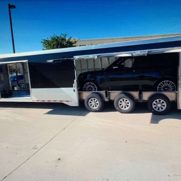 Large black car hauler trailer transporting a luxury vehicle in a parking lot.