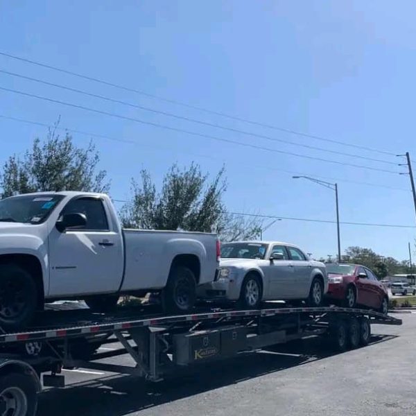 White pickup truck on a car transport trailer at a parking lot.