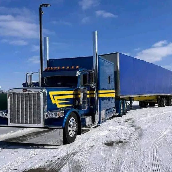 Blue semi-truck with trailer on snowy landscape for auto transport.